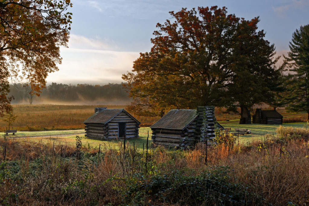 Cabane din busteni inconjurate de un camp cetos si frunzis de toamna in Parcul Istoric National Valley Forge, Pennsylvania